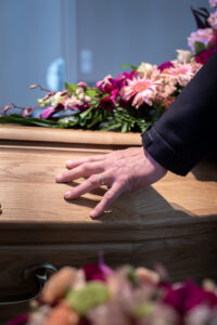 Main sur cercueil, fleurs en arrière-plan.