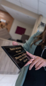 Femme tenant une plaque commémorative avec deux personnes.