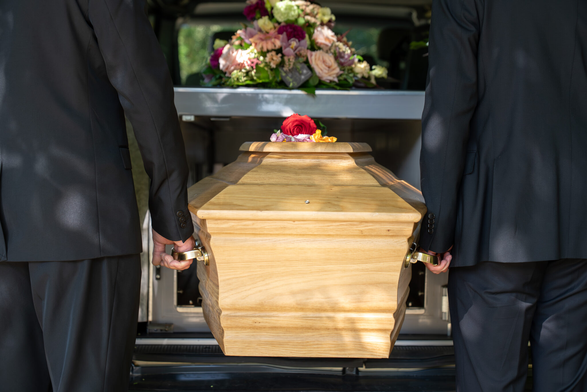 Cercueil en bois porté par deux personnes en costume.