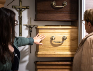 Deux femmes regardent des cercueils et crucifix.